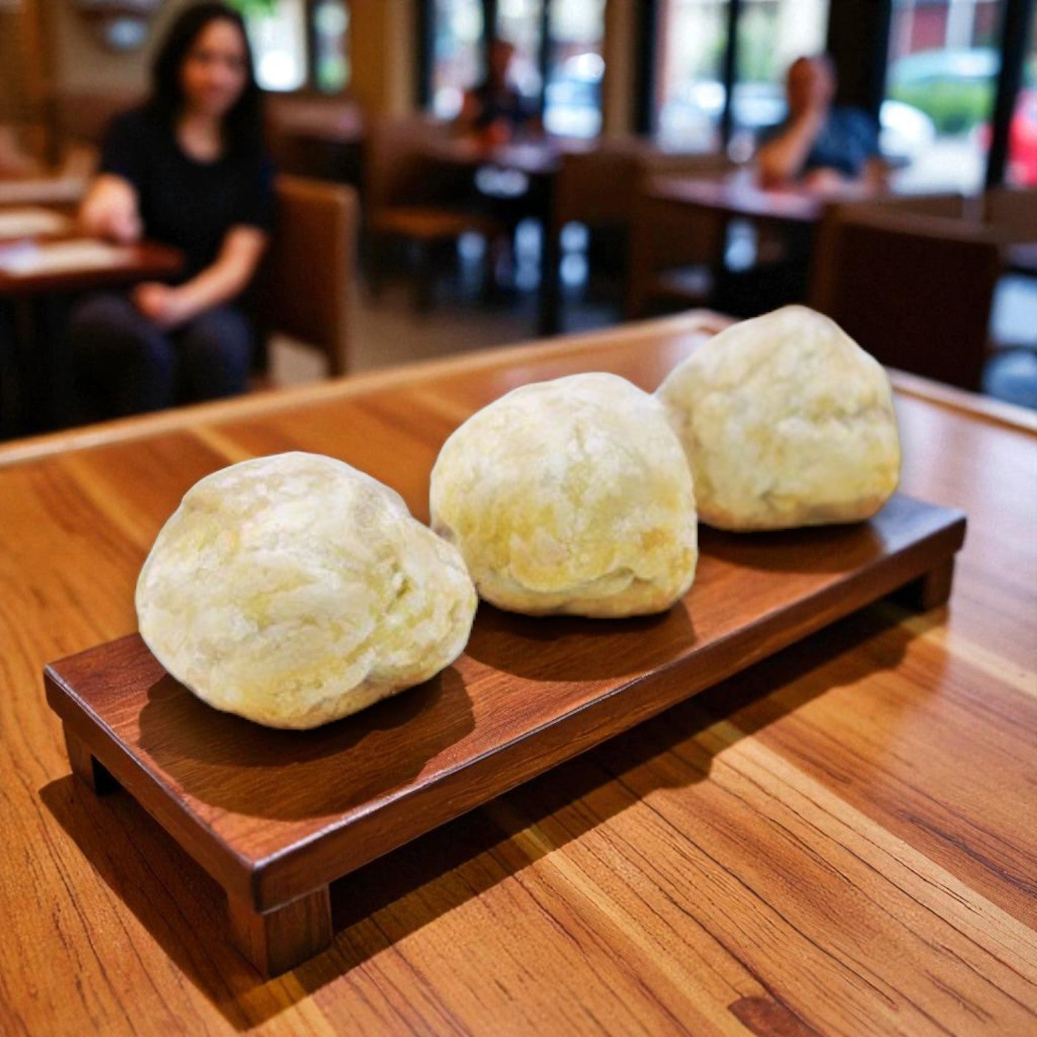 Three Van Lang Mini Beef Wellington appetizers are arranged in a row on a wooden tray atop a table, evoking the inviting presentation of premium frozen appetizers in a cozy restaurant setting.