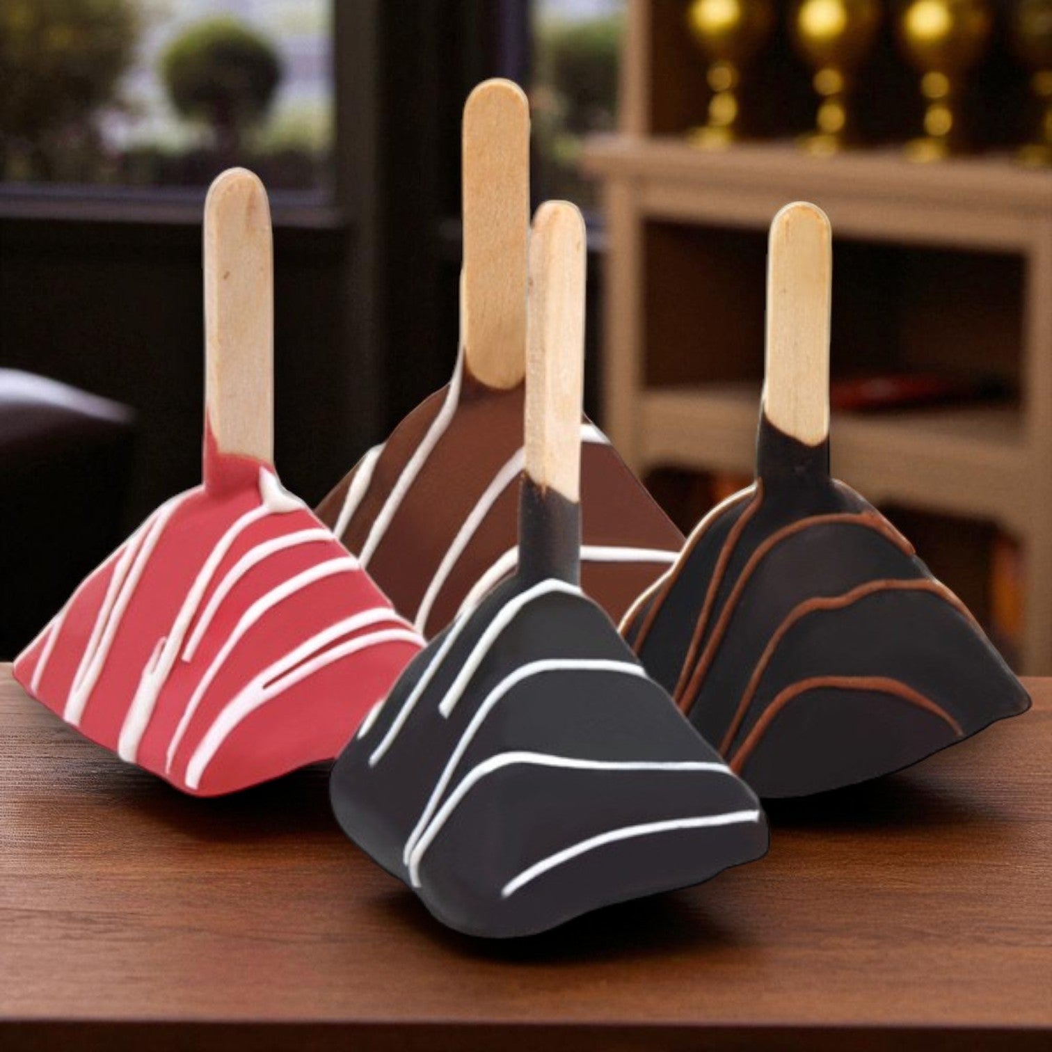 Van Lang Assorted Cheesecake Lollipops—chocolate-dipped, pyramid-shaped pops with white and brown drizzle on wooden sticks—are shown indoors on a wooden table. Each box contains 84 frozen desserts (2 trays of 42).