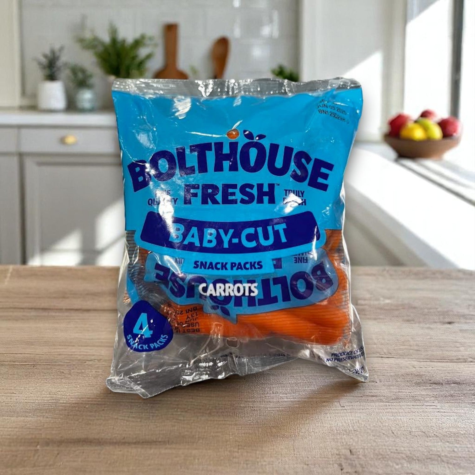 A Bolthouse Farms Carrots – 4 Pack rests on a kitchen counter, surrounded by fruit—ideal for fresh, healthy snacks from Bolthouse Farms.