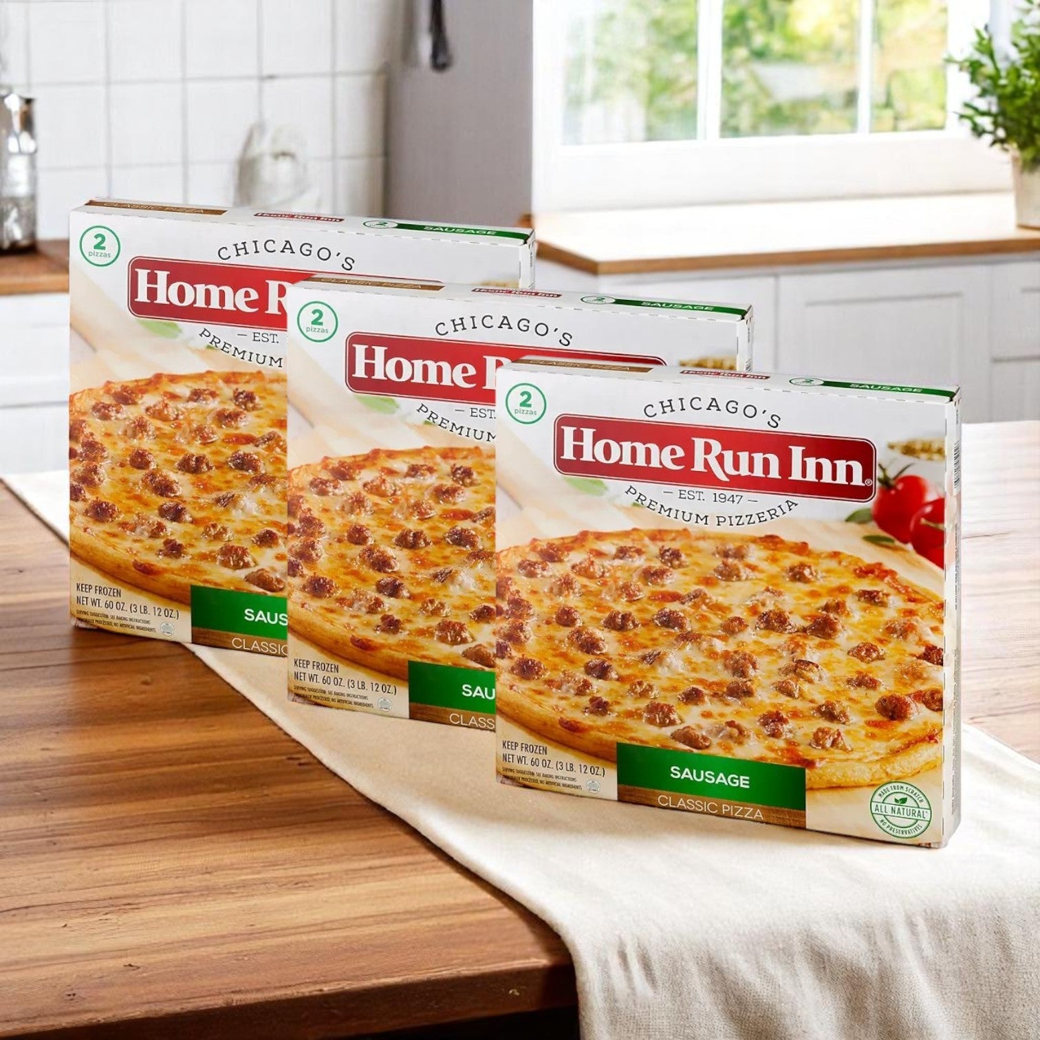 Three boxes of Home Run Inn Classic Sausage Pizza, 60 oz. - 3 Pack (6 total pizzas), are displayed on a kitchen counter with a white table runner.