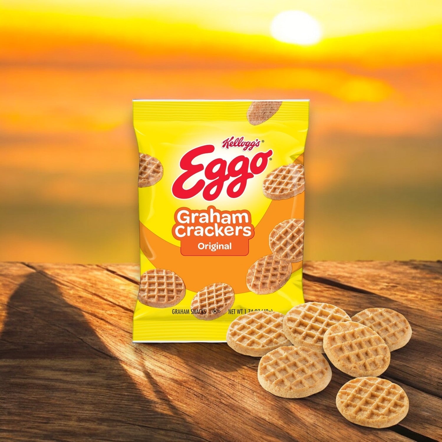 A package of Kellogg's Cracker Graham Eggo Waffle - 100 Pack (1.74 oz Each) rests on a wooden surface with waffles scattered around, echoing a homestyle ambiance against a blurred sunset backdrop.