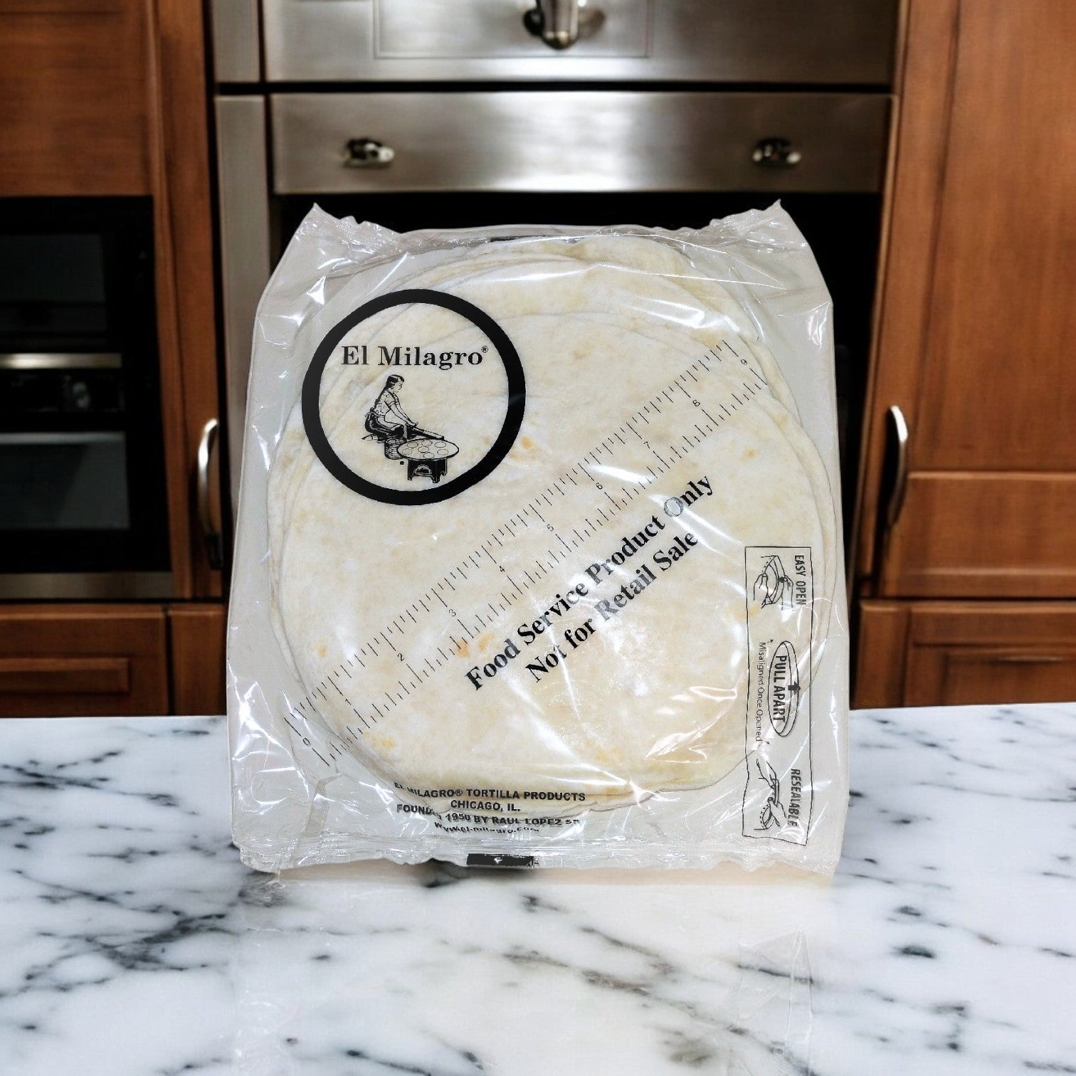 On a marble countertop, a package of El Milagro Flour Tortillas - 8-Inch - 20 Packs of 12 Dozen is labeled "Food Service Product Only," promising an authentic taste for culinary creations, with an elegantly framed kitchen cabinet in the background.