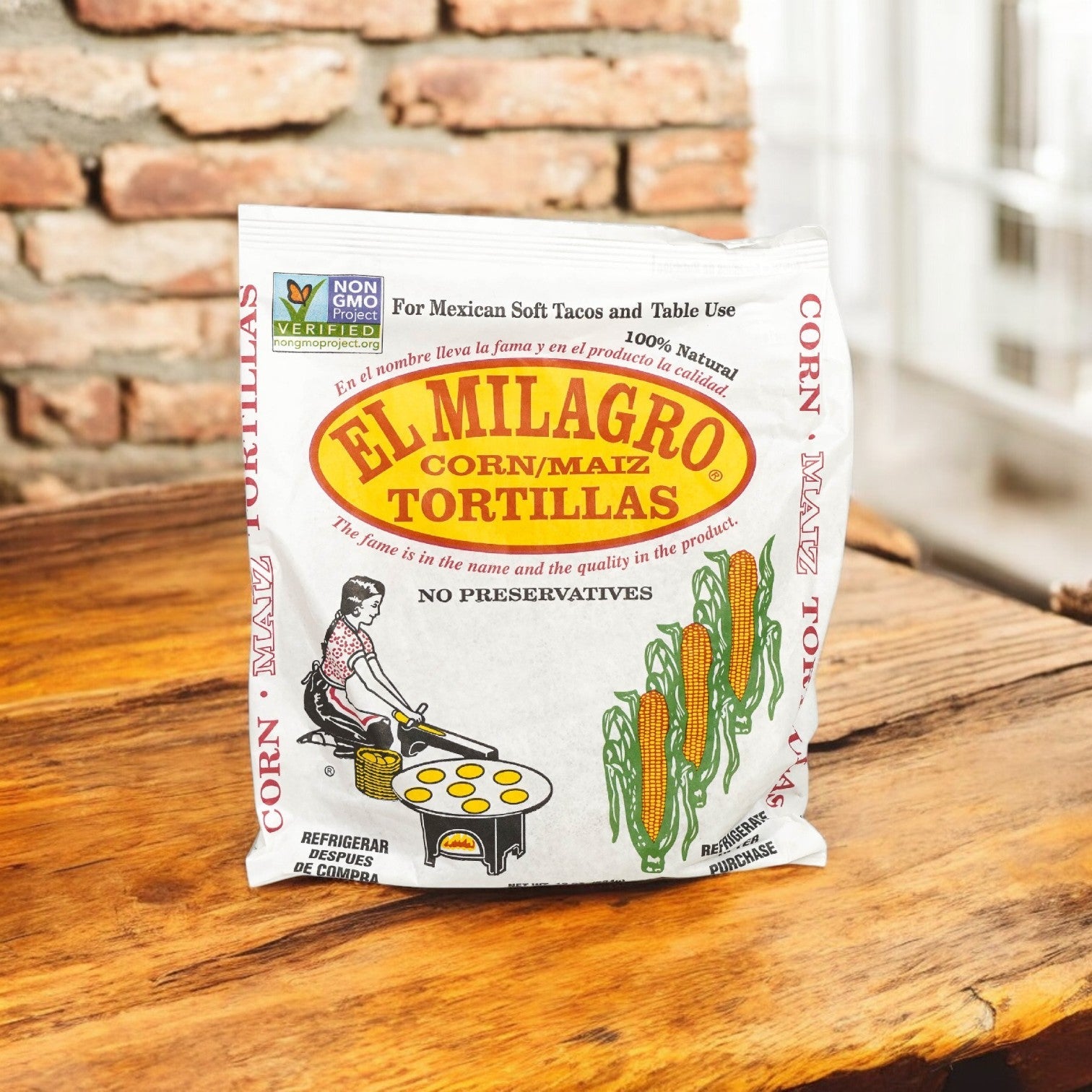 El Milagro Yellow Corn Tortillas - 6", in packs of 40 dozen, rest on a wooden surface against a brick backdrop. The packaging emphasizes non-GMO verification, no preservatives, and corn imagery with tortilla preparation for authentic Mexican flavor and versatile size enjoyment.