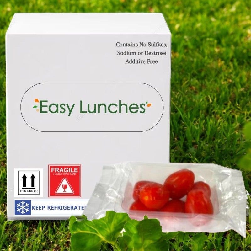An Easy Lunches package in white lies on the grass, with a small sealed bag of fresh Grape Tomatoes (2.5 oz.) beside it.