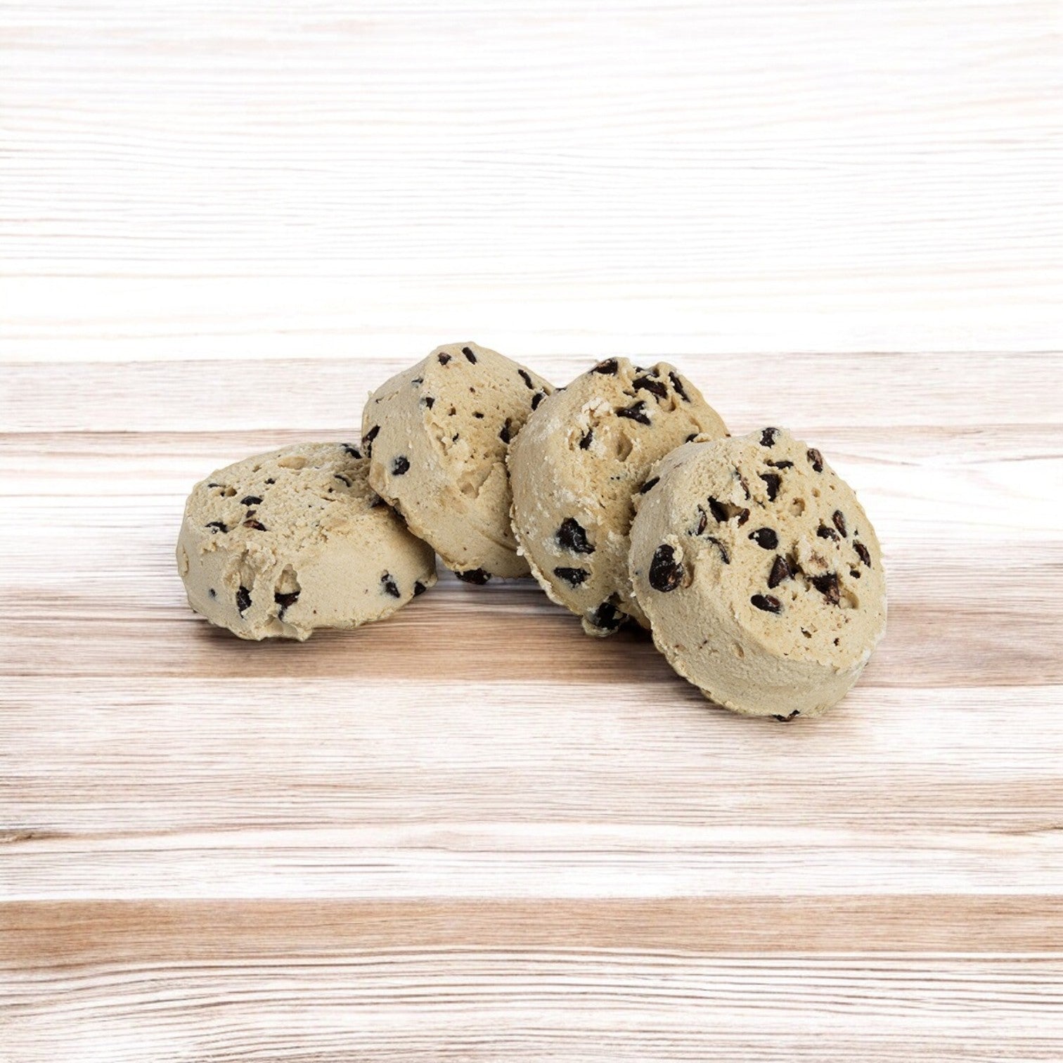 Four scoops of Otis Spunkmeyer Dough Cookie Chocolate Chip 80/4 oz. rest invitingly on a wooden surface.