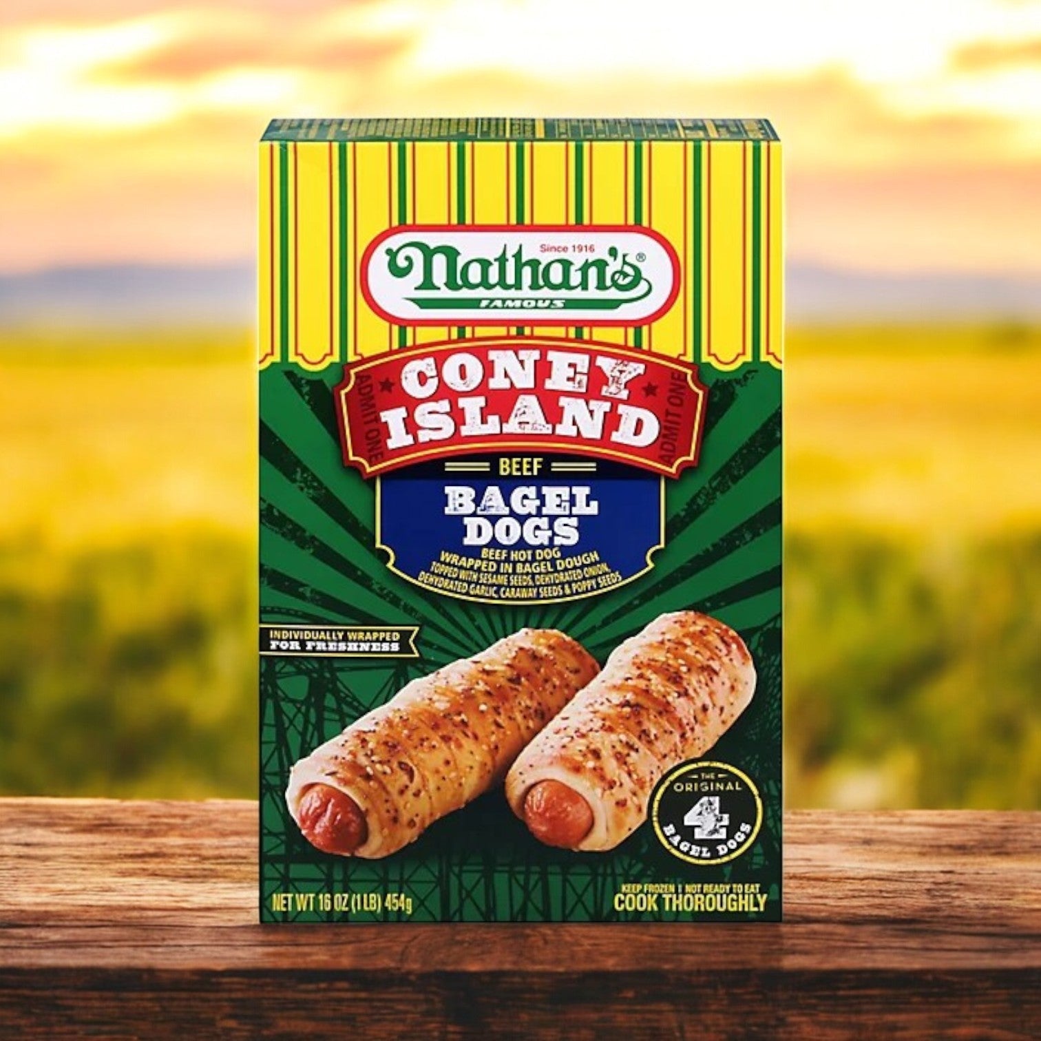A 20 oz box of Nathan’s Famous Coney Island Bagel Dogs, showcasing premium beef hot dogs, sits on a wooden surface with a blurred outdoor backdrop.