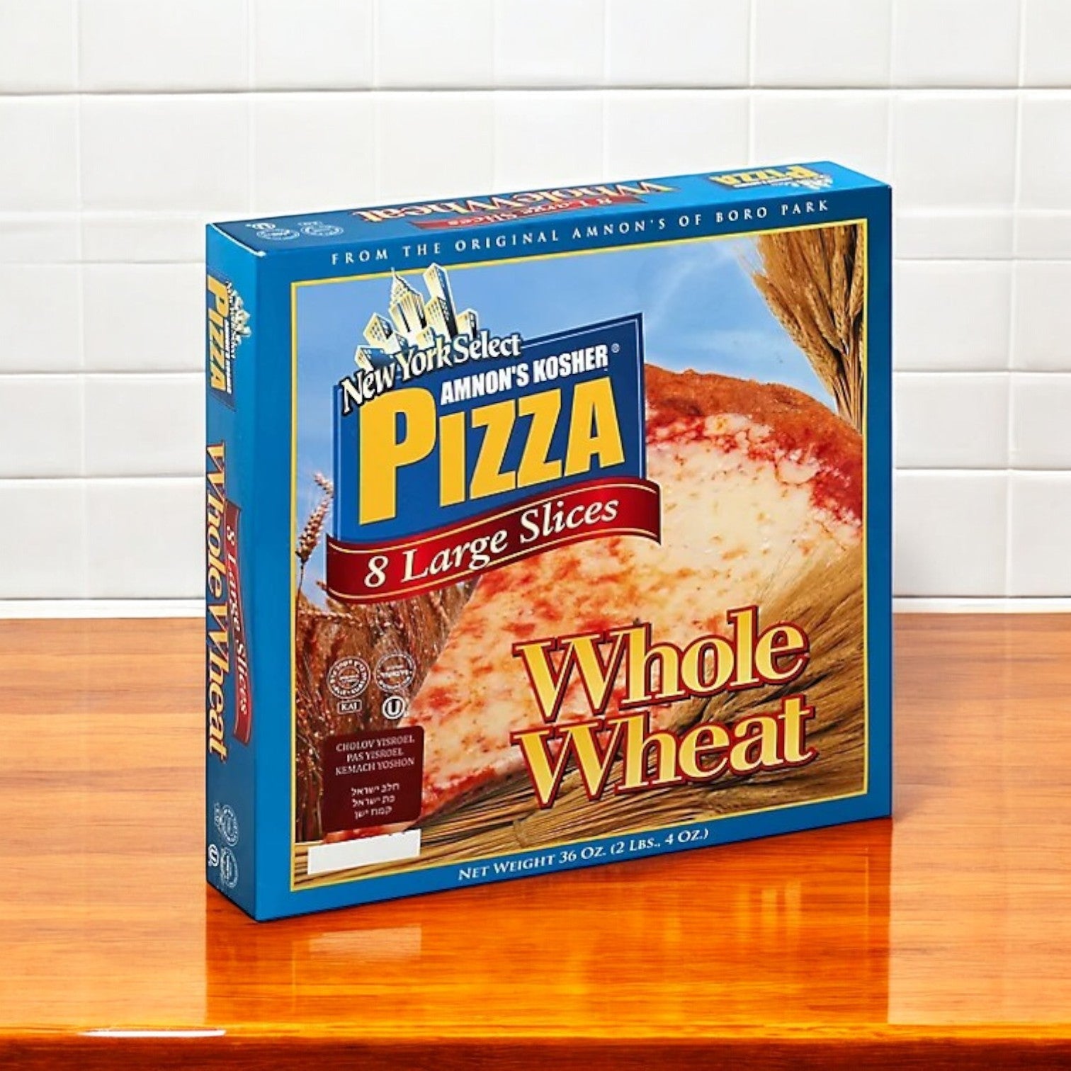A box of Amnon's Kosher Pizza Whole Wheat Frozen 36 oz. sits on a wooden counter, offering 8 large slices with a 100% whole wheat crust.