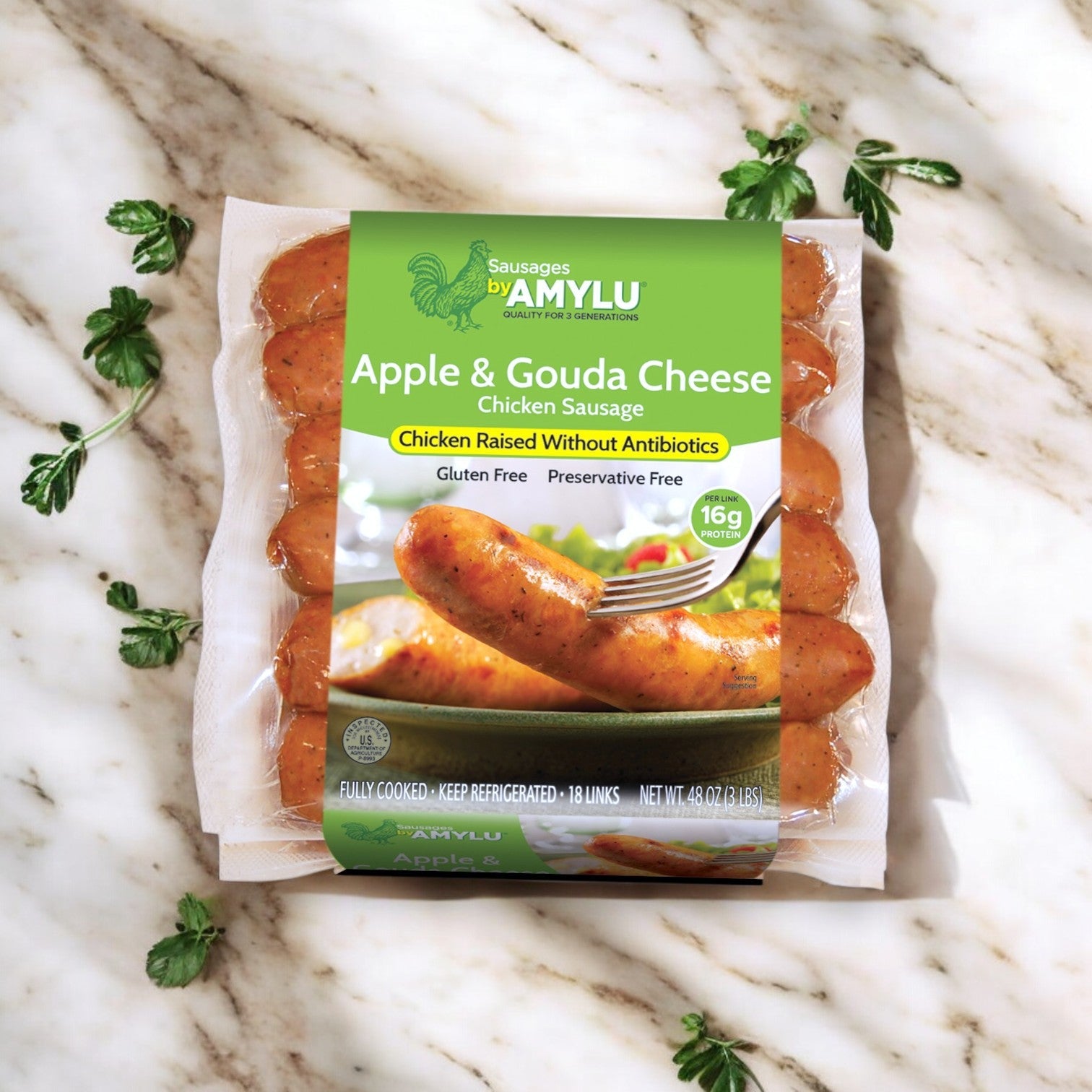A package of Amylu Apple & Gouda Cheese Chicken Sausage (3 lbs, 18 ct) sits on a marble surface. The label showcases its gourmet appeal, emphasizing gluten-free and preservative-free qualities with premium chicken raised without antibiotics.