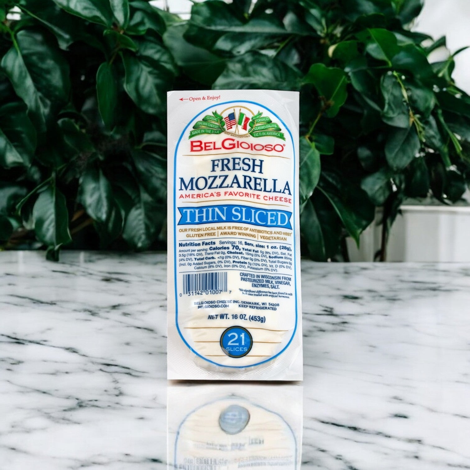 A package of Belgioioso Fresh Mozzarella Cheese Thin Sliced – 8/1 LB with 21 slices of premium mozzarella elegantly rests on a marble surface, green foliage in the background.