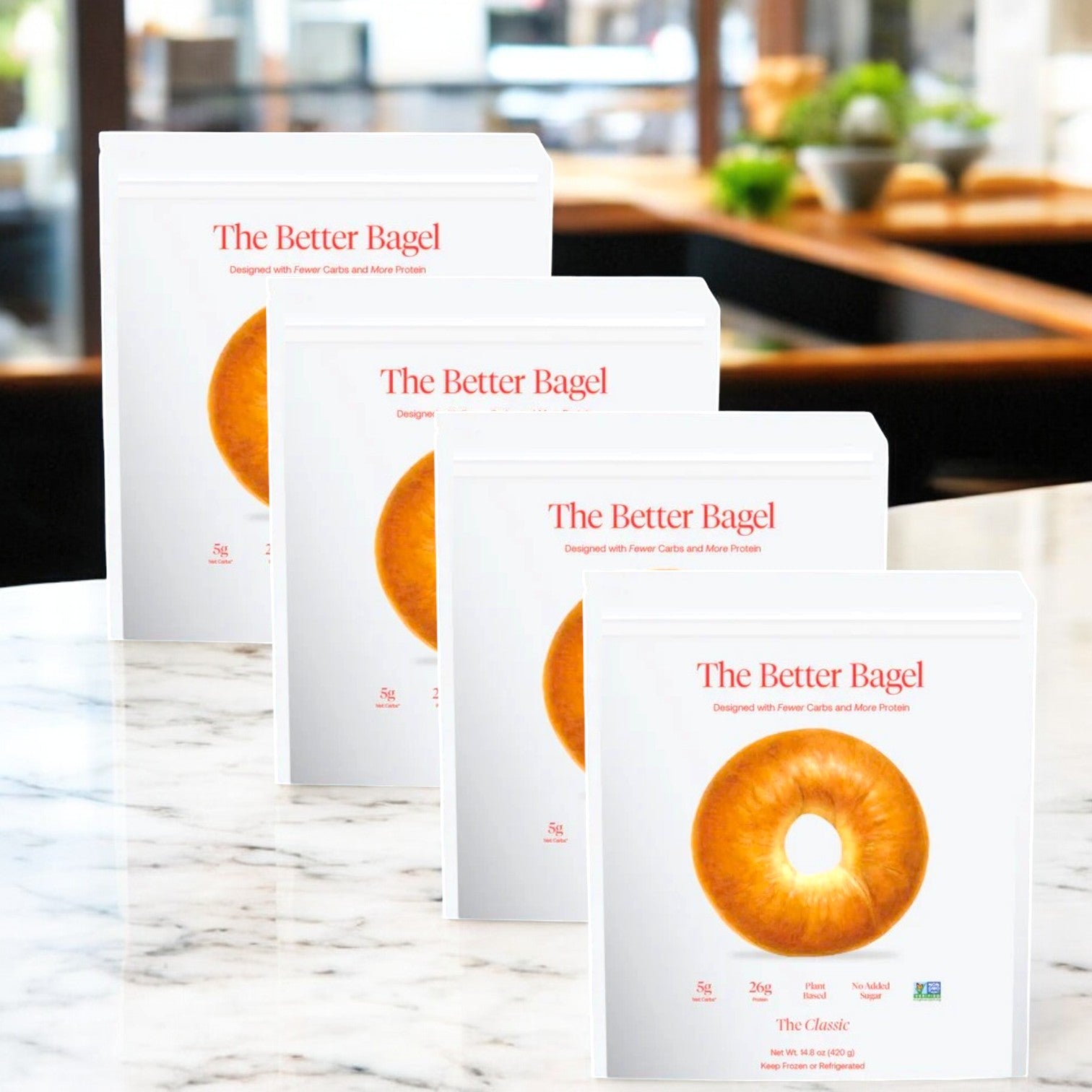 Four boxes of "The Classic Better Bagel" are on a marble table, each with an image of a breakfast bagel and text promoting their low carb and high protein design. Sold as "BetterBrand - The Classic Better Bagel - 4 Bags, 16 Total Bagels!" in stock and ready to ship!.