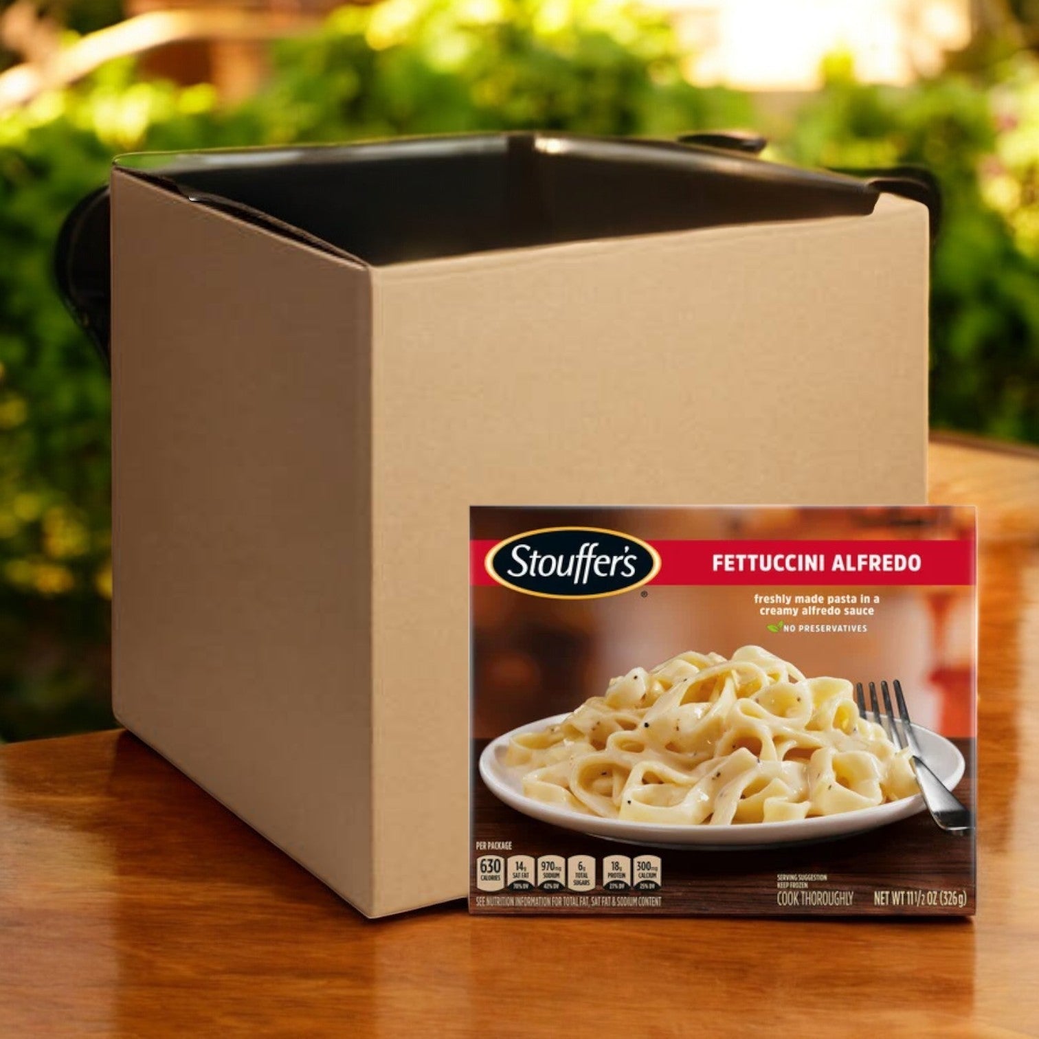 An enticing package of Stouffer's Fettuccini Alfredo, 11.5 oz. - 8 Count, rests invitingly in front of a plain cardboard box on a wooden surface.