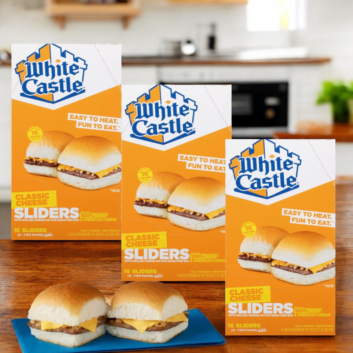 Three boxes of White Castle Microwaveable Frozen Cheeseburger Sliders-29.28 Oz are displayed on a kitchen counter, while two sliders rest enticingly on a blue plate.