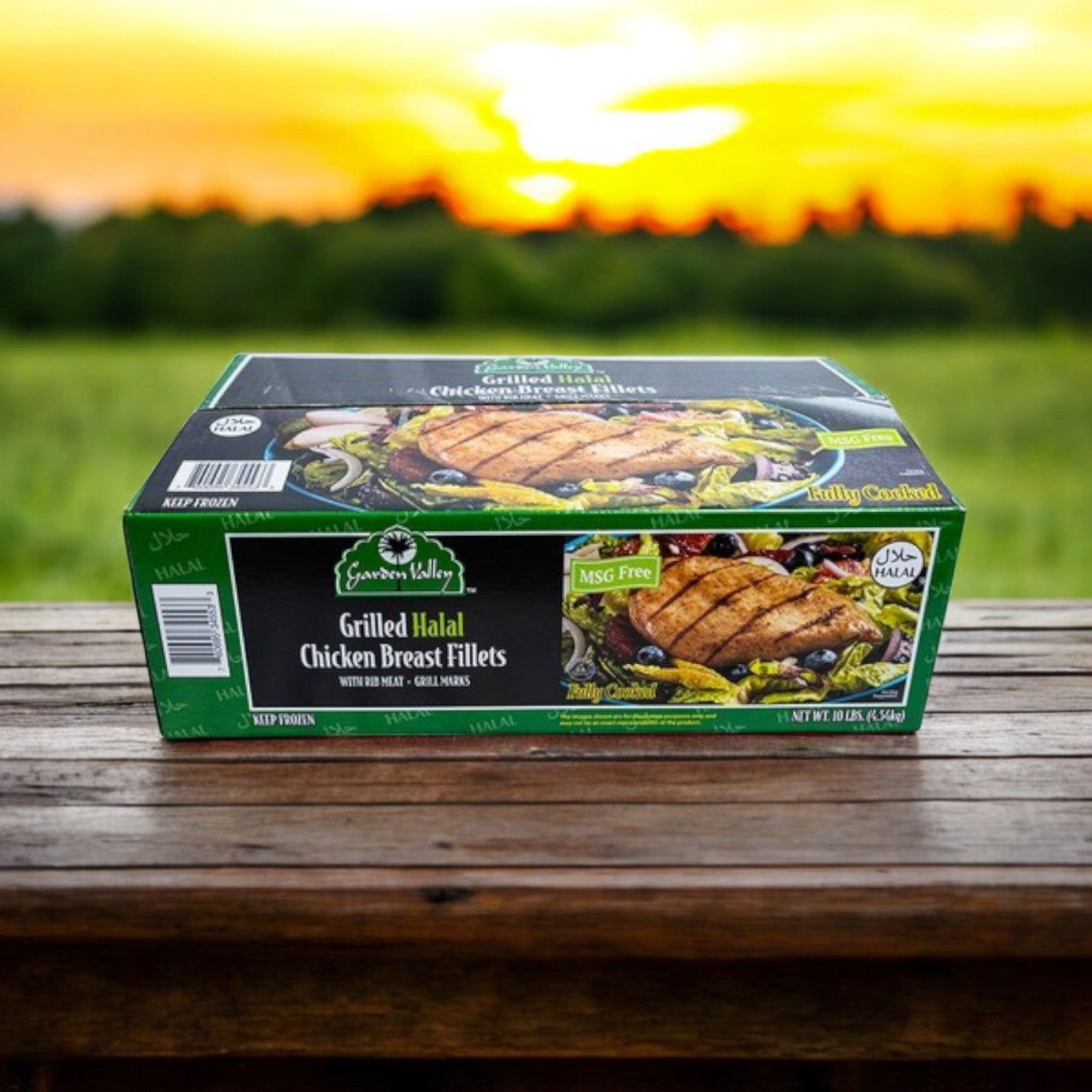 A box of Garden Valley Grilled Halal Chicken Breast Fillets, Fully Cooked – 10 lbs, sits on a wooden surface with a sunset and blurred greenery in the background.