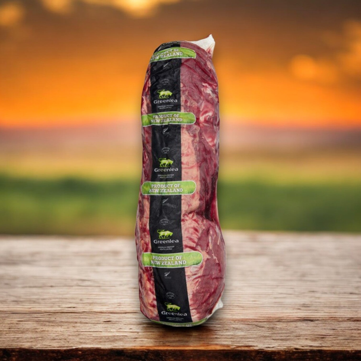 A packaged cut of Halal Beef Tenderloin, 6 lb Avg, from Silver Fern Farms sits on a wooden surface against a blurred sunset landscape, highlighting its premium quality.