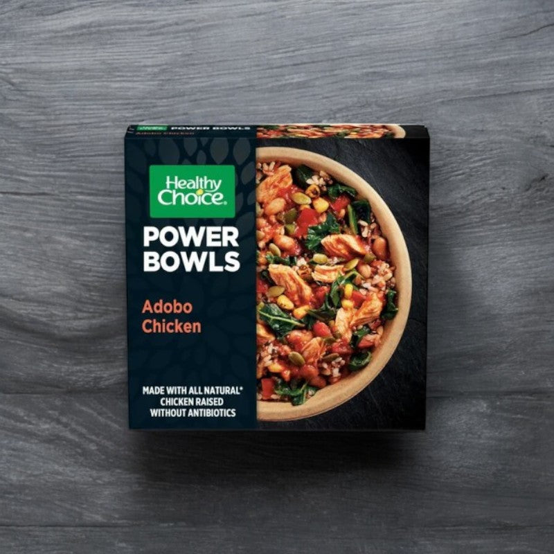 A box of Healthy Choice Power Bowls Chicken Adobo, 9.75 oz., by Healthy Choice is shown against a gray background, emphasizing its use of all-natural chicken raised without antibiotics.