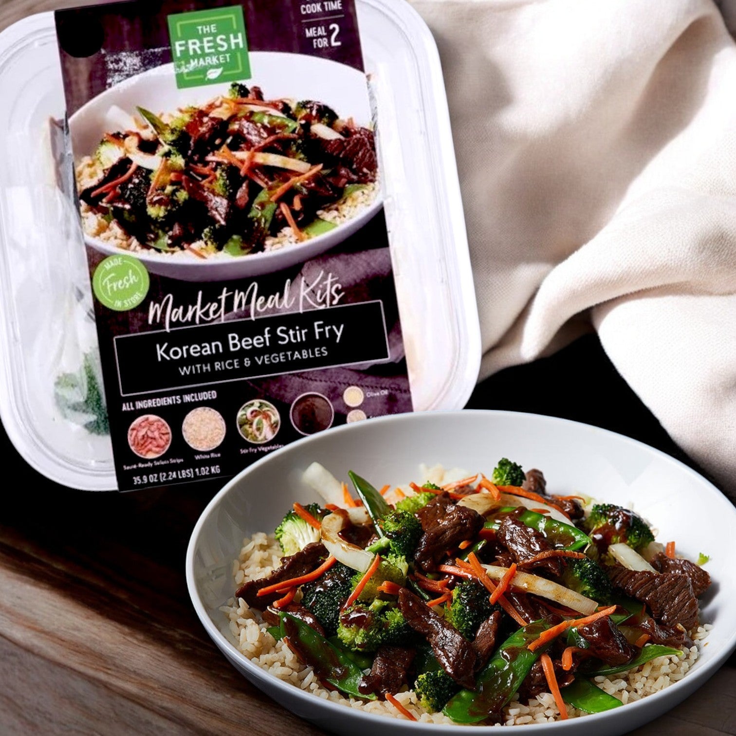 The Fresh Market Korean Beef Stir Fry with Fresh Vegetables & Rice Market Meal Kit – 36 oz packs authentic flavors, offering a delectable dish of beef, broccoli, carrots, and rice served beautifully on a white plate.