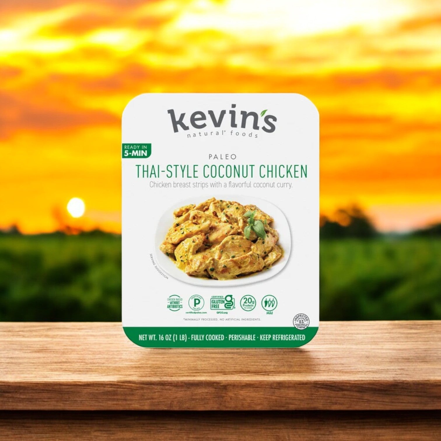 The packaging of Kevin's Thai-Style Coconut Chicken 1 Box - 16 oz features a sunset over a peaceful field, reflecting the authentic Thai spices infused in its creamy coconut sauce.