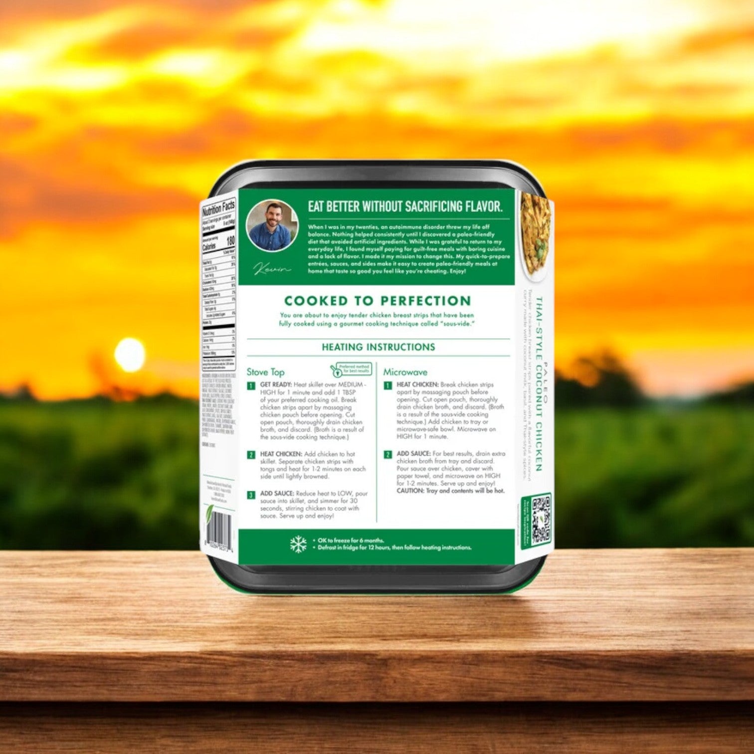 A box of Kevin's Thai-Style Coconut Chicken (16 oz) on a wooden surface with a field behind it. The packaging features cooking instructions, a QR code, and hints of authentic Thai spices, adding an exotic twist to each comforting bowl.
