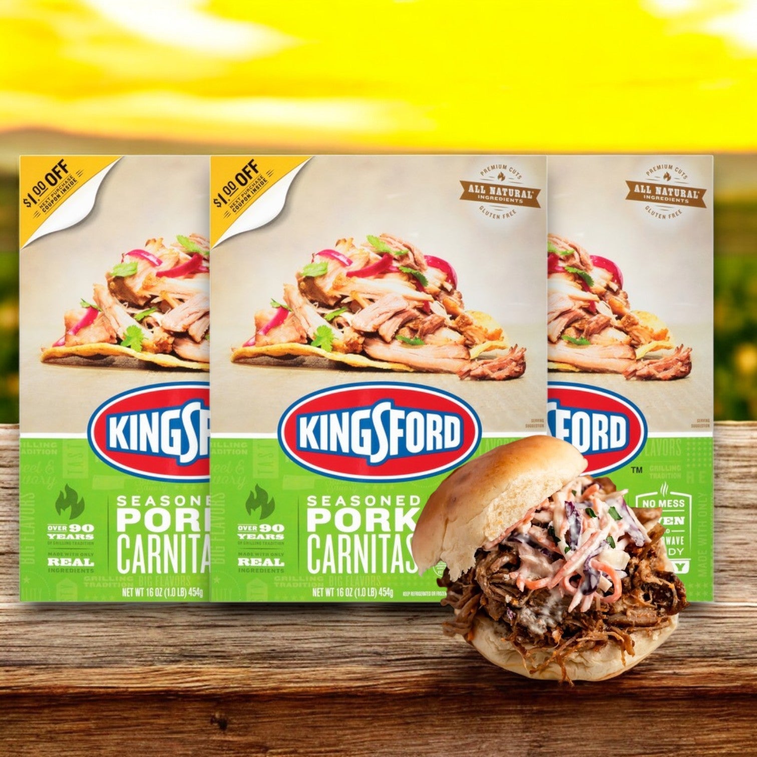In front of a sunny landscape sits a box of Kingsford Seasoned Pork Carnitas – 16 oz -3 Count, perfectly slow-cooked and ready, with a sandwich showcasing the smoky-seasoned pork.