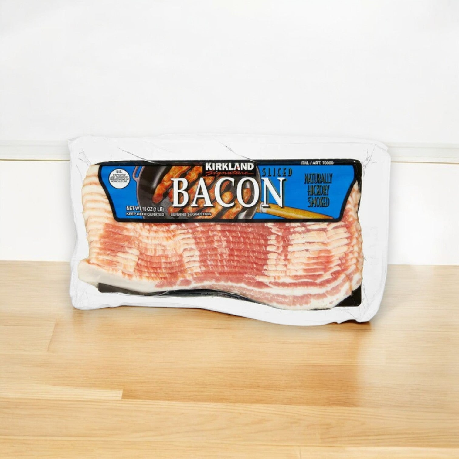 A pack of Kirkland Signature Bacon, Hickory Smoked, rests on wood, featuring images of perfectly cooked bacon and a blue label. Ideal for breakfast, it promises a deliciously savory start to your day.