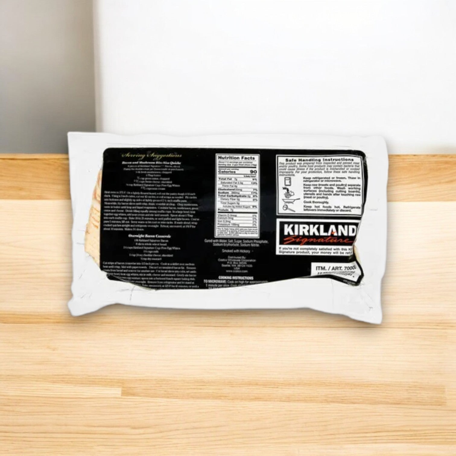 A pack of Kirkland Signature Hickory Smoked Bacon sits on wood, its black label showcasing nutritional facts and branding. Ideal for breakfast, it guarantees rich flavor in each slice.