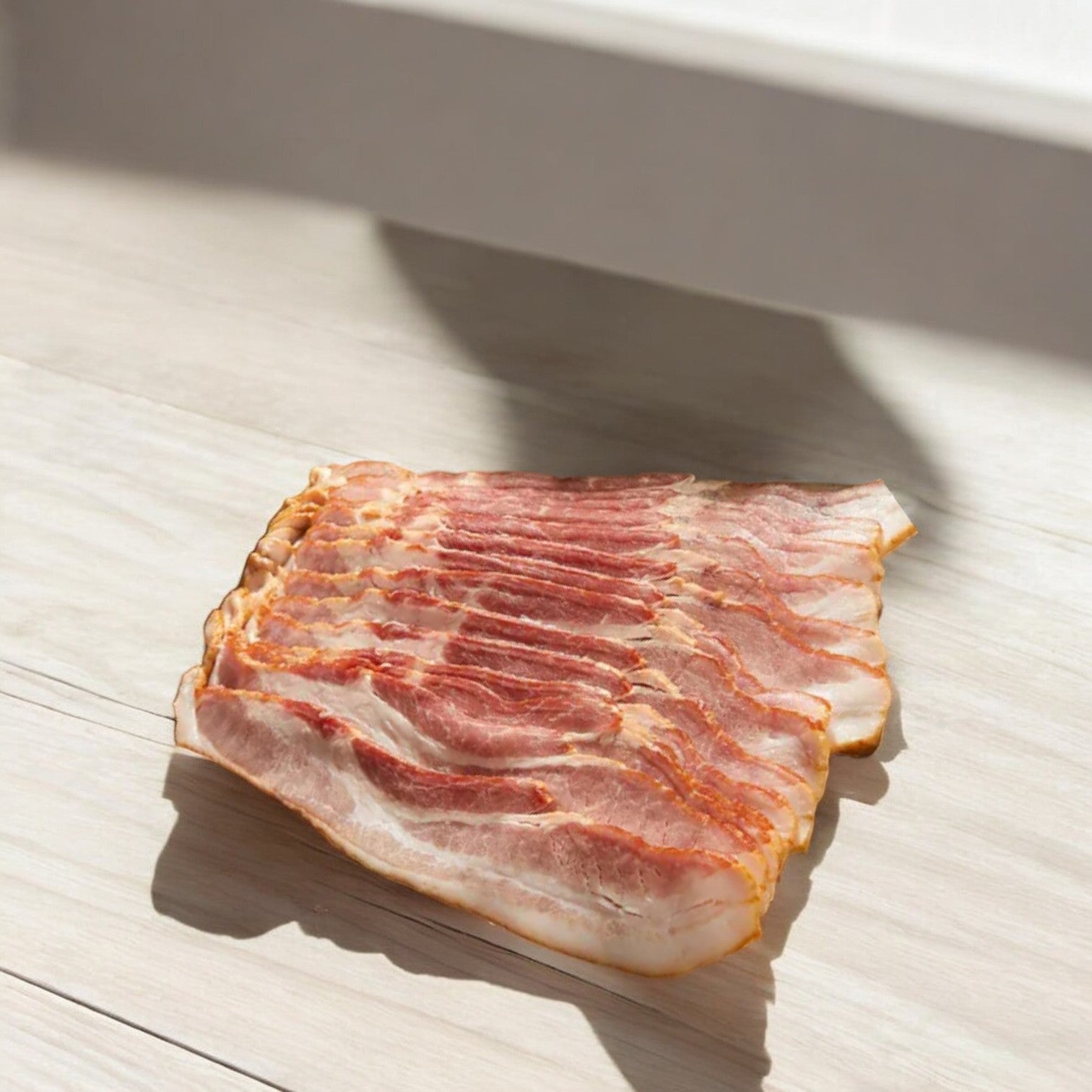 Slices of Kirkland Signature Hickory Smoked Bacon gleam under sunlight on a light wooden surface.
