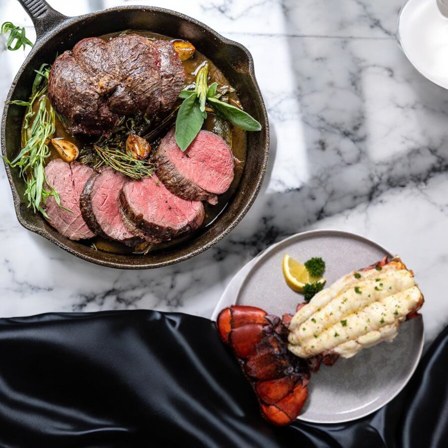 The Easy Lunches "Surf and Turf!" features USDA Choice Beef Loin Tenderloin Steak reminiscent of filet mignon, paired with succulent frozen Netuno lobster tails, presented elegantly with a lemon wedge on marble and black cloth.