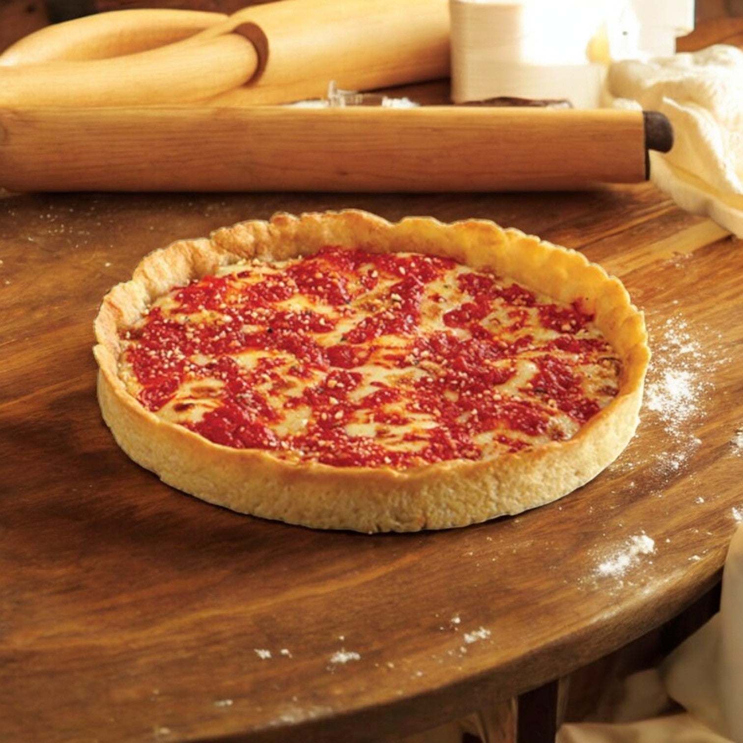 A Lou Malnati's Deep Dish Pizza Cheese, 23 oz., topped with rich tomato sauce and gooey mozzarella cheese sits on a wooden surface, surrounded by rolling pins and flour.