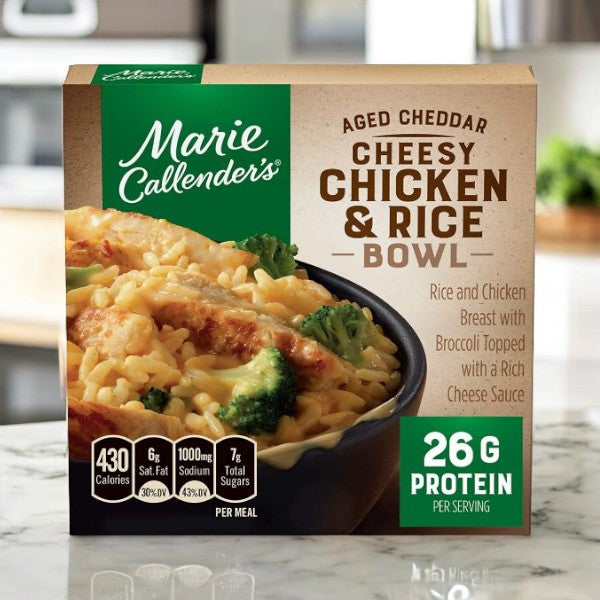 Marie Callender's Meals Bundle, featuring 8 meals including Aged Cheddar Cheesy Chicken & Rice Bowl, is shown on a kitchen counter. This meal includes broccoli and cheese with 26g protein and 430 calories, with packaging detailing fat, sodium, and sugar content.