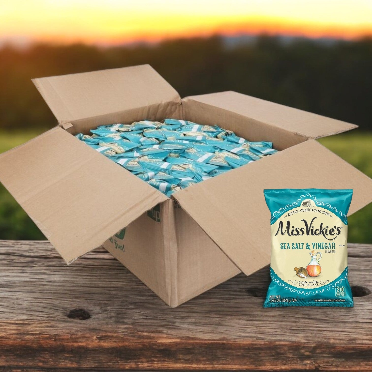 A bag of Miss Vickie's Potato Chips Salted & Vinegar Kettle 64/1.375 oz. rests on a wooden surface with a few crispy chips in front, set against a blurred sunset background, highlighting the bold flavors in every bite.