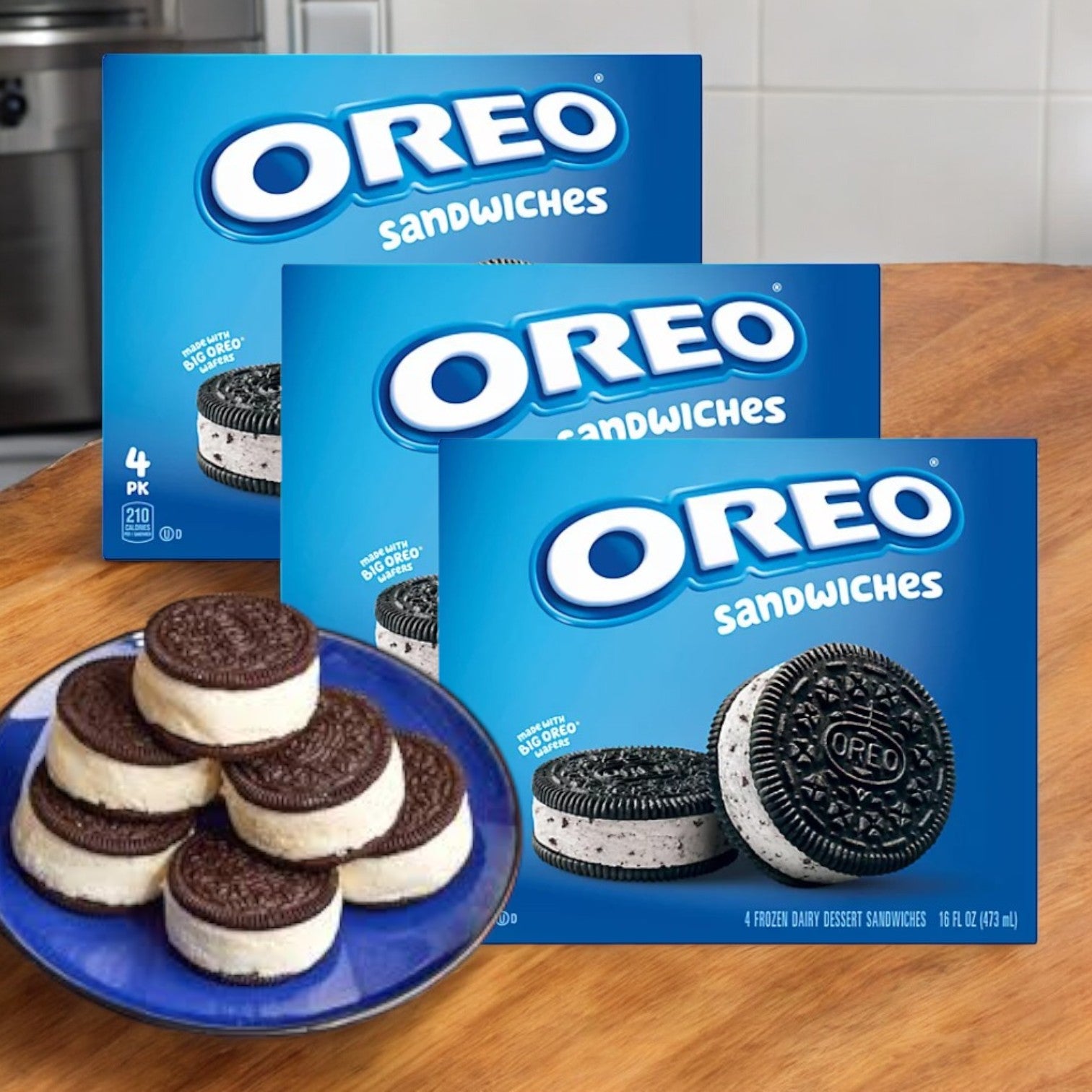 Behind a blue plate stacked with Oreo Dairy Dessert Sandwiches, three Nabisco boxes promise a delightful frozen treat adventure, each containing four creamy sandwiches.