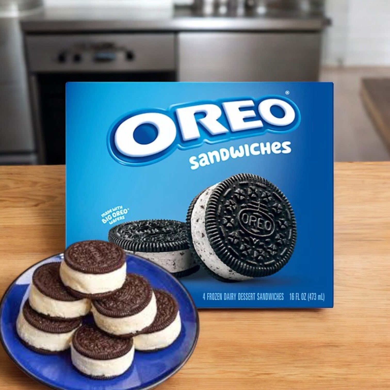 A Nabisco Oreo Dairy Dessert Sandwiches box sits on a kitchen counter, accompanied by a plate stacked with four individually wrapped frozen sandwiches.