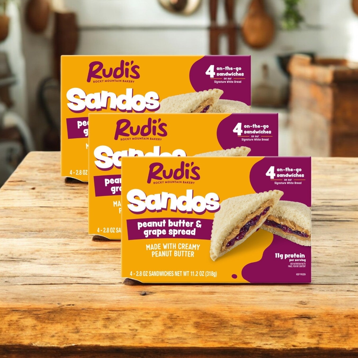 Rudi's Rocky Mountain Bakery's Peanut Butter and Grape Spread Sandos, 11.2 oz - 3 Packs are displayed on a wooden table.
