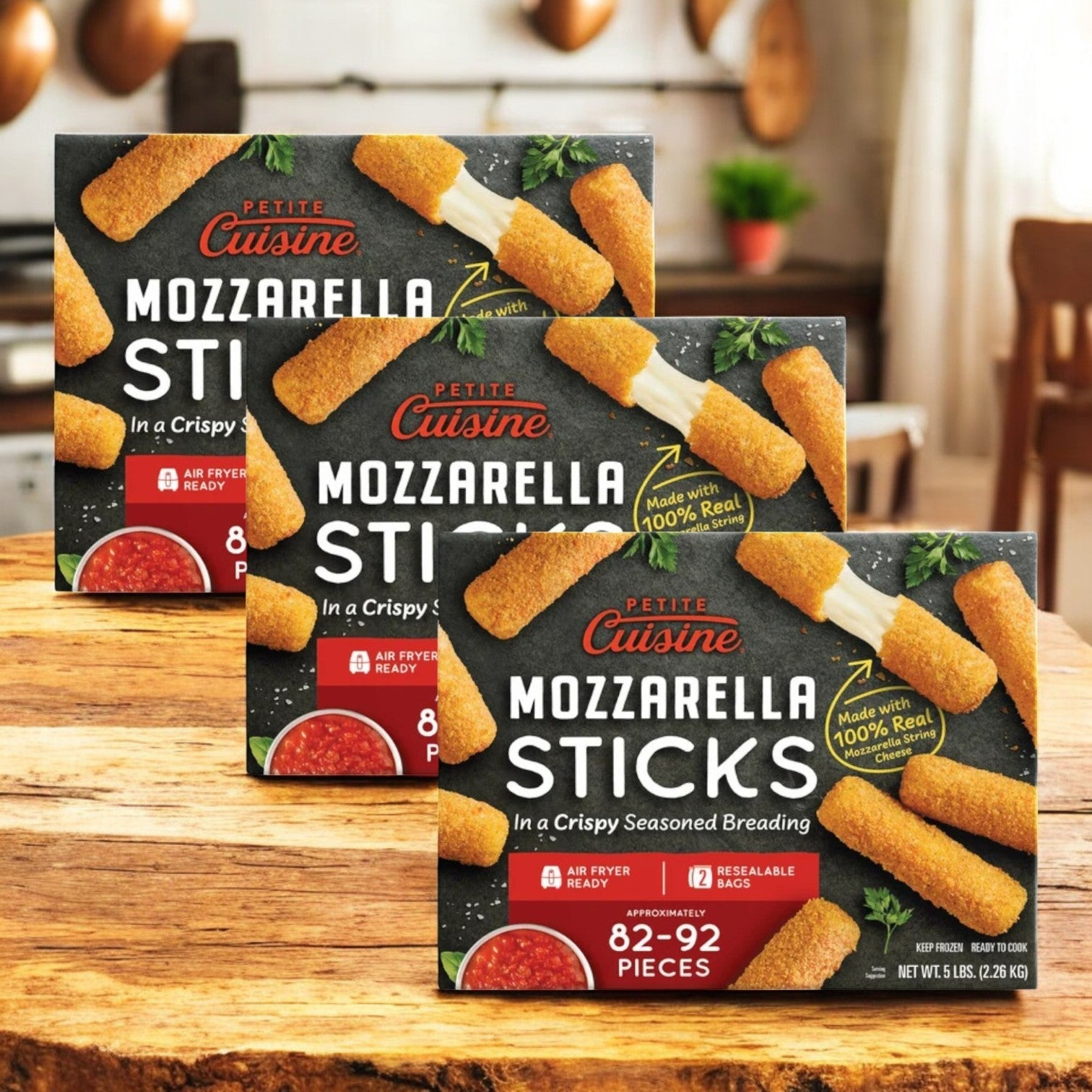 Petite Cuisine Mozzarella Sticks, 5 lb-3 Count, are displayed on a wooden kitchen surface. Each box offers 82-92 crispy pieces made with 100% real mozzarella cheese, neatly packaged in sealed bags.