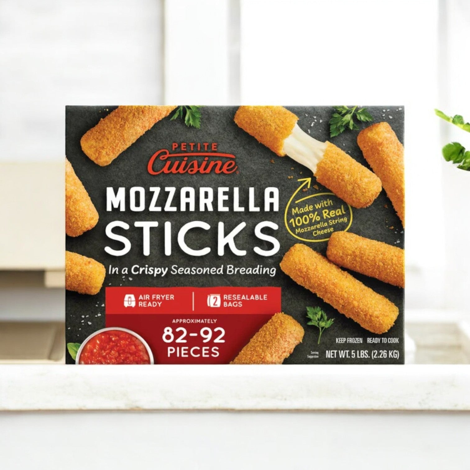 A 5 lb box from Petite Cuisine containing 82-92 mozzarella sticks sits on the counter. These air fryer-ready treats feature seasoned breading with a crispy coating and real mozzarella cheese, all in reclosable bags for freshness.