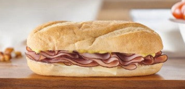 A freshly prepared sub sandwich from Easy Lunches' Sandwich Variety Pack, featuring layers of sliced ham and cheese, rests on a wooden surface—ideal for office lunches. Ships frozen with a 30-day shelf life once thawed!.