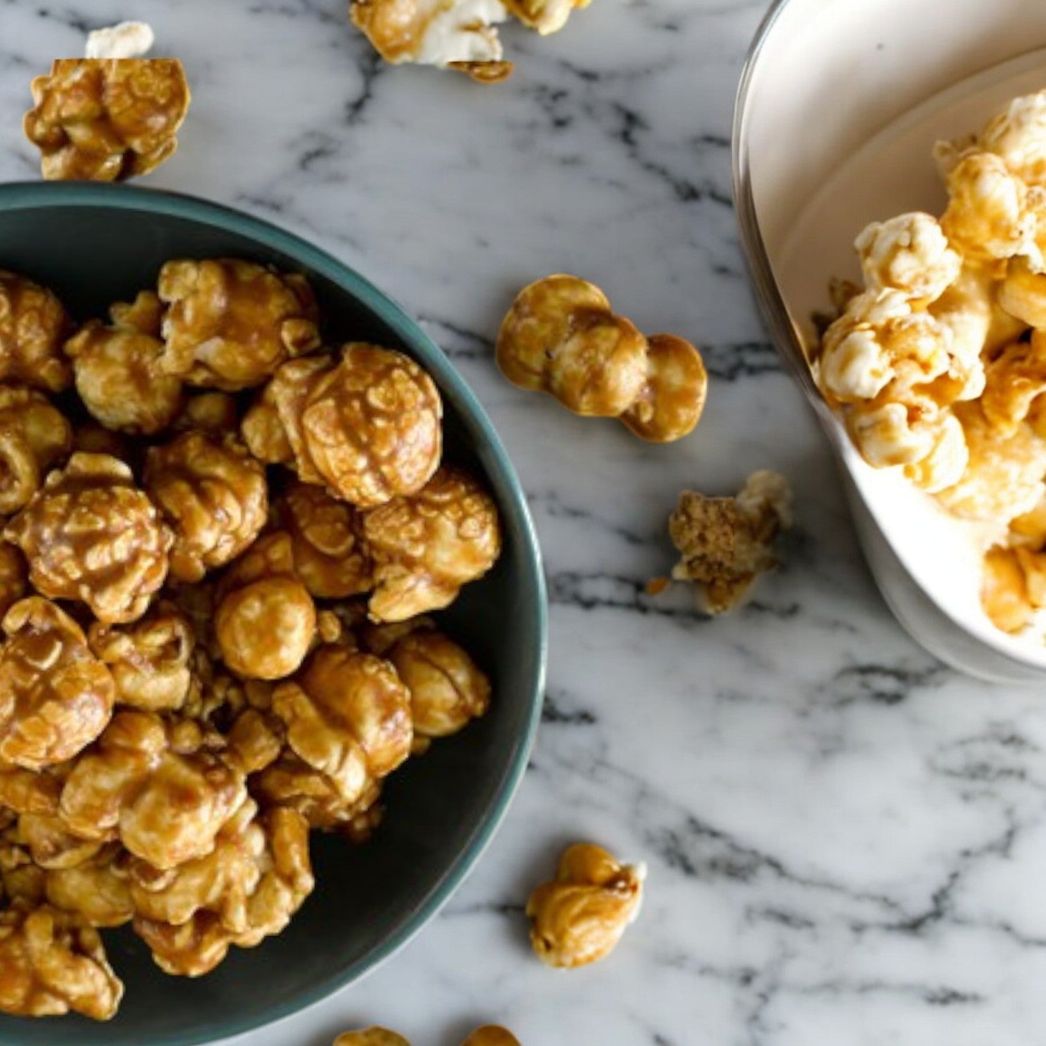 Garrett's CaramelCrisp® popcorn, from their Classic Tin size with 14 cups, alongside plain popcorn on a marble surface, scattered pieces evoking its classic charm.