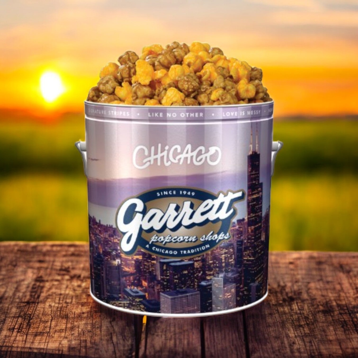 The Garrett Popcorn tin, featuring a Chicago cityscape and filled with 14 cups of the Garrett Mix, blends CaramelCrisp and CheeseCorn. It rests on a wooden table, set against the soft colors of a sunset.