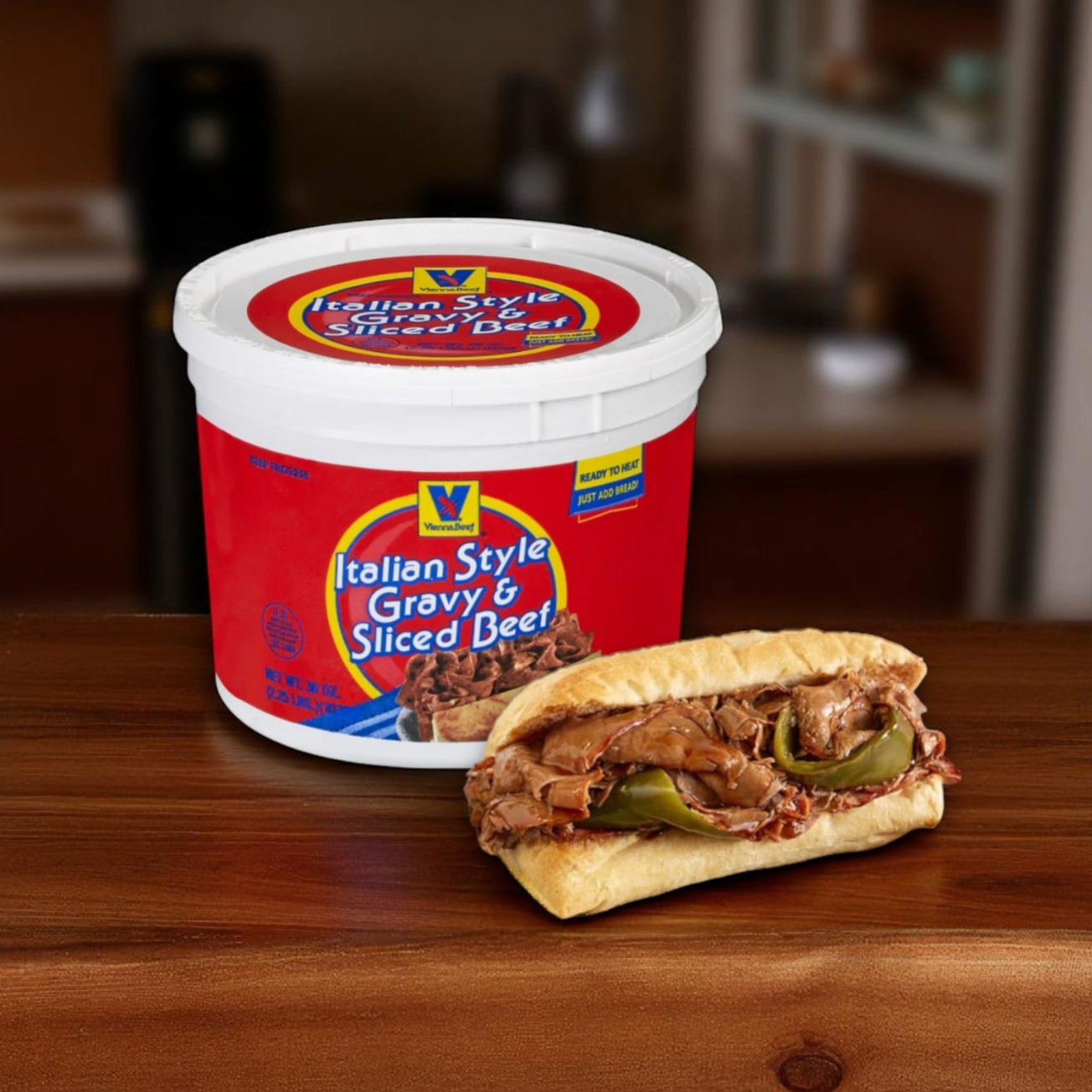 A Vienna Beef® Authentic Chicago Sandwich Kit, featuring Italian Style Gravy & Sliced Beef and Turano® French Rolls, sits behind a sandwich filled with sliced beef and green peppers on a wooden surface.