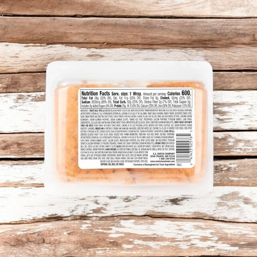 A plastic container with E.A. Sween's Turkey Club Wrap—featuring turkey, bacon, ham, cheddar, and ranch—rests on a wooden surface. The detailed label highlights the flavor-boosting crispy bacon ingredients and key nutrition facts.