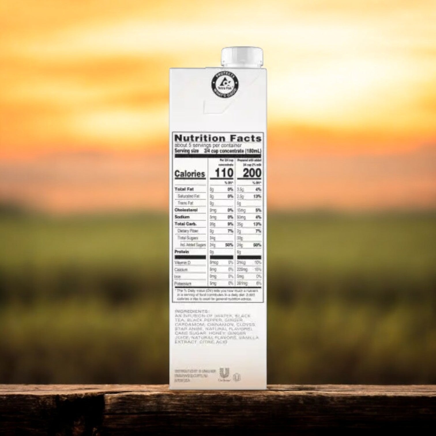A carton of Tazo Tea Chai Classic Concentrate - 6/32 oz, highlighting its nutrition facts and ingredients label, sits elegantly on a wooden surface against a blurred landscape backdrop, inviting you to enjoy its rich black tea blend.