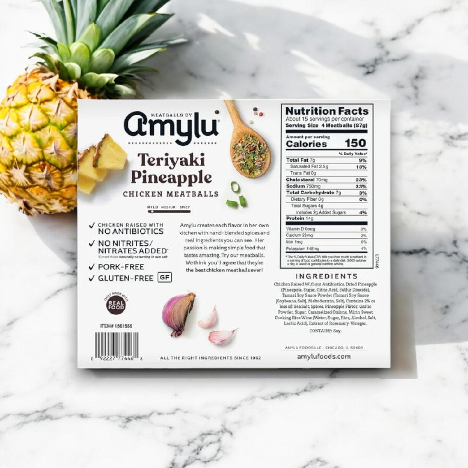 The 46 oz Amylu Teriyaki Pineapple Chicken Meatballs are elegantly displayed on a marble surface, highlighting premium ingredients like antibiotic-free chicken. Nearby, pineapple and garlic emphasize the savory blend in these flavorful meatballs.