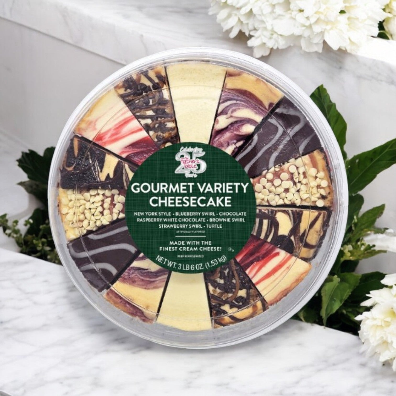 A round 10-inch, 14-slice cheesecake by The Father's Table, featuring premium pre-sliced flavors such as New York, blueberry, chocolate, raspberry, brownie, strawberry, and turtle varieties, is elegantly displayed on a white surface alongside flowers.