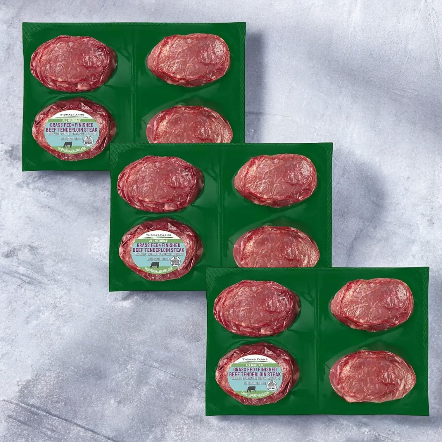 The Thomas Farms Tenderloin Beef Steak package features three packs of grass-fed beef tenderloin steaks, artfully placed on a textured surface. Each pack includes four vacuum-sealed steaks, offering a total of 12 premium cuts. Ideal for gourmet dining, these exceptional steaks promise a luxurious culinary experience and come with free shipping.