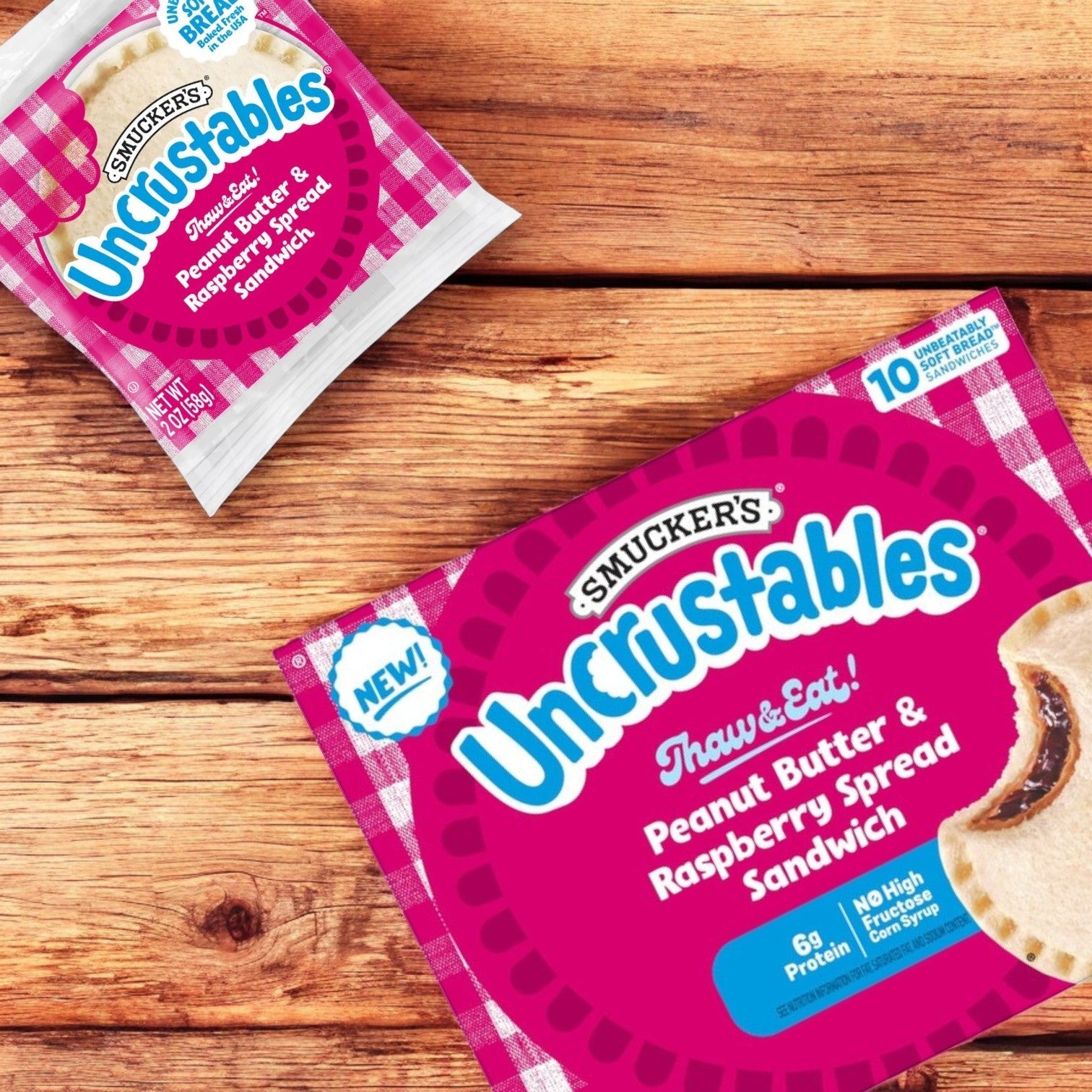 Two packages of Uncrustable Smuckers are on a wooden surface; the larger box is an Uncrustables Combo of 3, featuring ten peanut butter and raspberry spread sandwiches made with crustless bread.