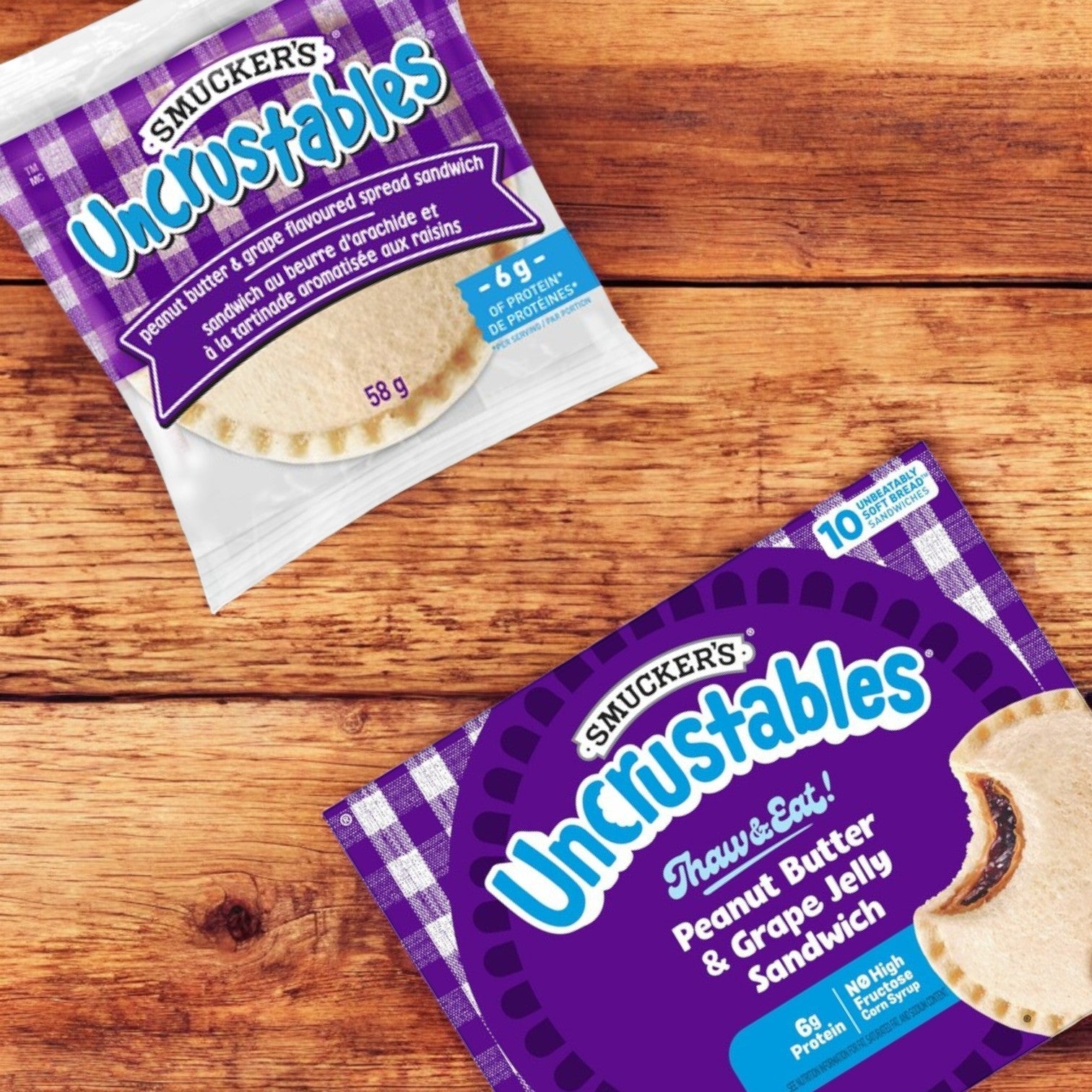 On a wooden surface sit two Smucker's Uncrustables packages: a single pack and a 10-count box featuring peanut butter and grape jelly sandwiches on crustless bread, known as the Uncrustables Combo of 3 – 10 Count Each from Uncrustable Smuckers. Perfect for those seeking an Uncrustables Combo delight.