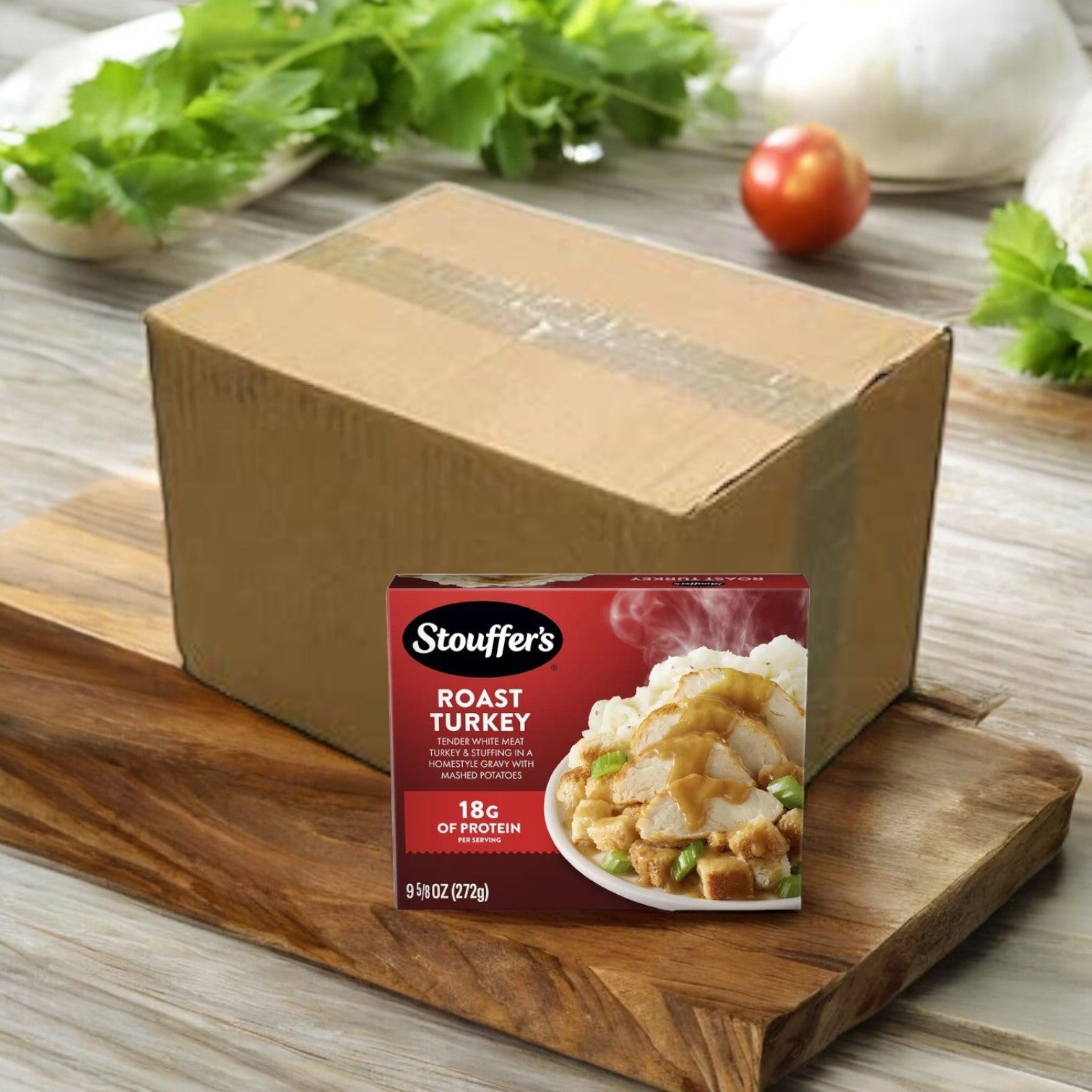 A Stouffer's Roast Turkey frozen meal box, part of the 8-count, 9.625 oz package, sits on a wooden board with creamy mashed potatoes; fresh vegetables are nearby as a large cardboard box looms in the background.