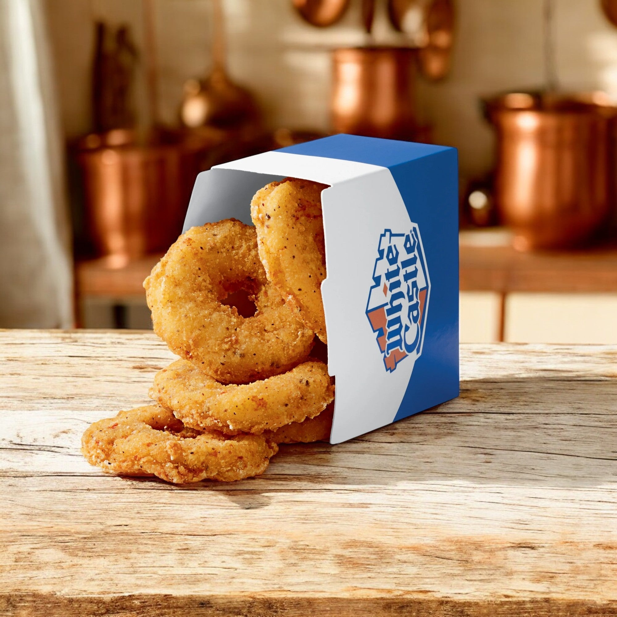 A White Castle 3 Pack Combo! box of onion rings tips over onto a wooden surface in a cozy setting.