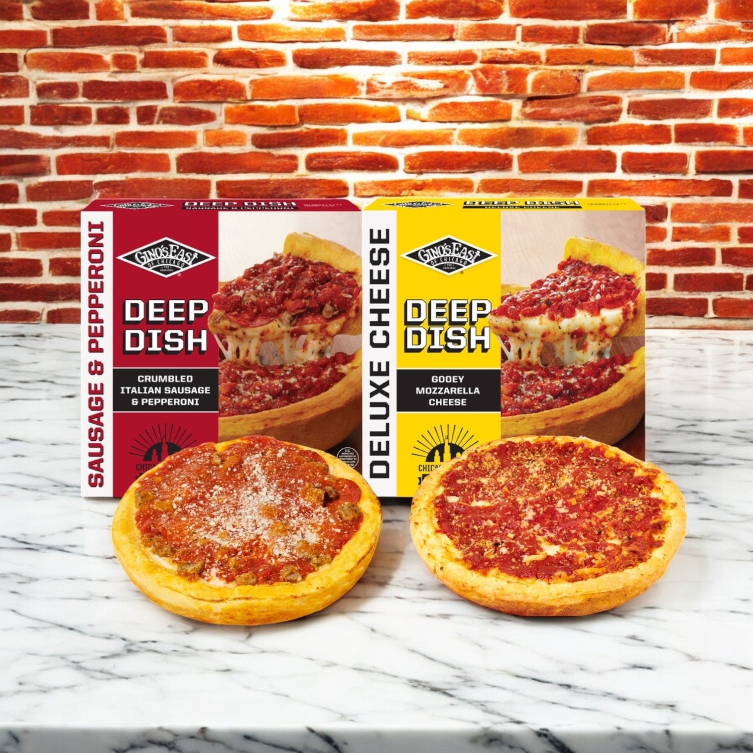 Two Gino's East- 2 Pack Combo! pizzas, one with sausage and pepperoni and the other a deluxe cheese, rest on a marble surface. Their matching boxes are set in front of a brick wall.