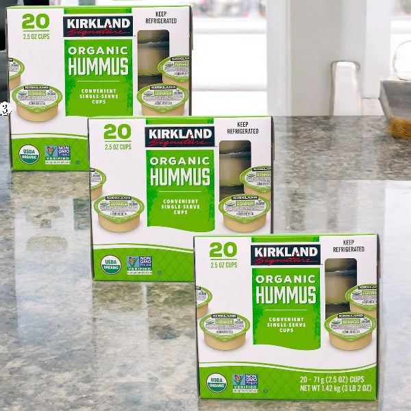Three cases of Kirkland Signature Organic Hummus, each with 20 cups and rich in creamy tahini and premium chickpeas, are elegantly displayed on a marble countertop.